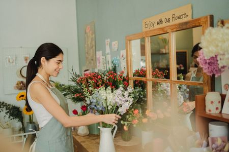 Woman arranging flowers in a bright floral shop with vases and bouquets.