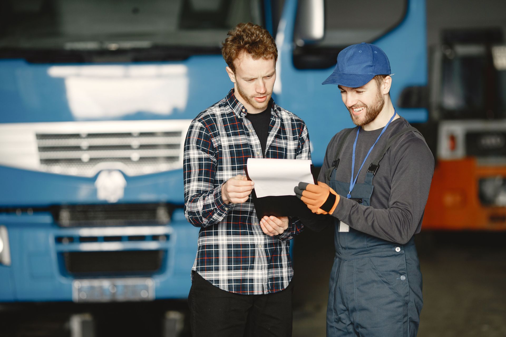 Two mechanics reviewing paperwork in front of a blue truck in a garage