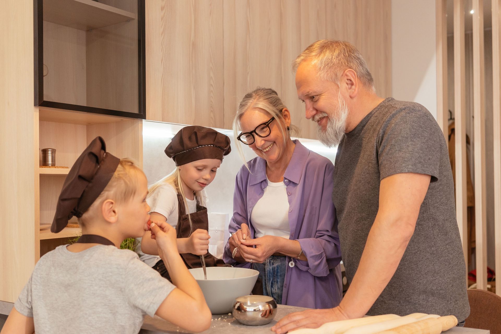 Family baking together in a bright kitchen, smiling around a bowl and mixing ingredients