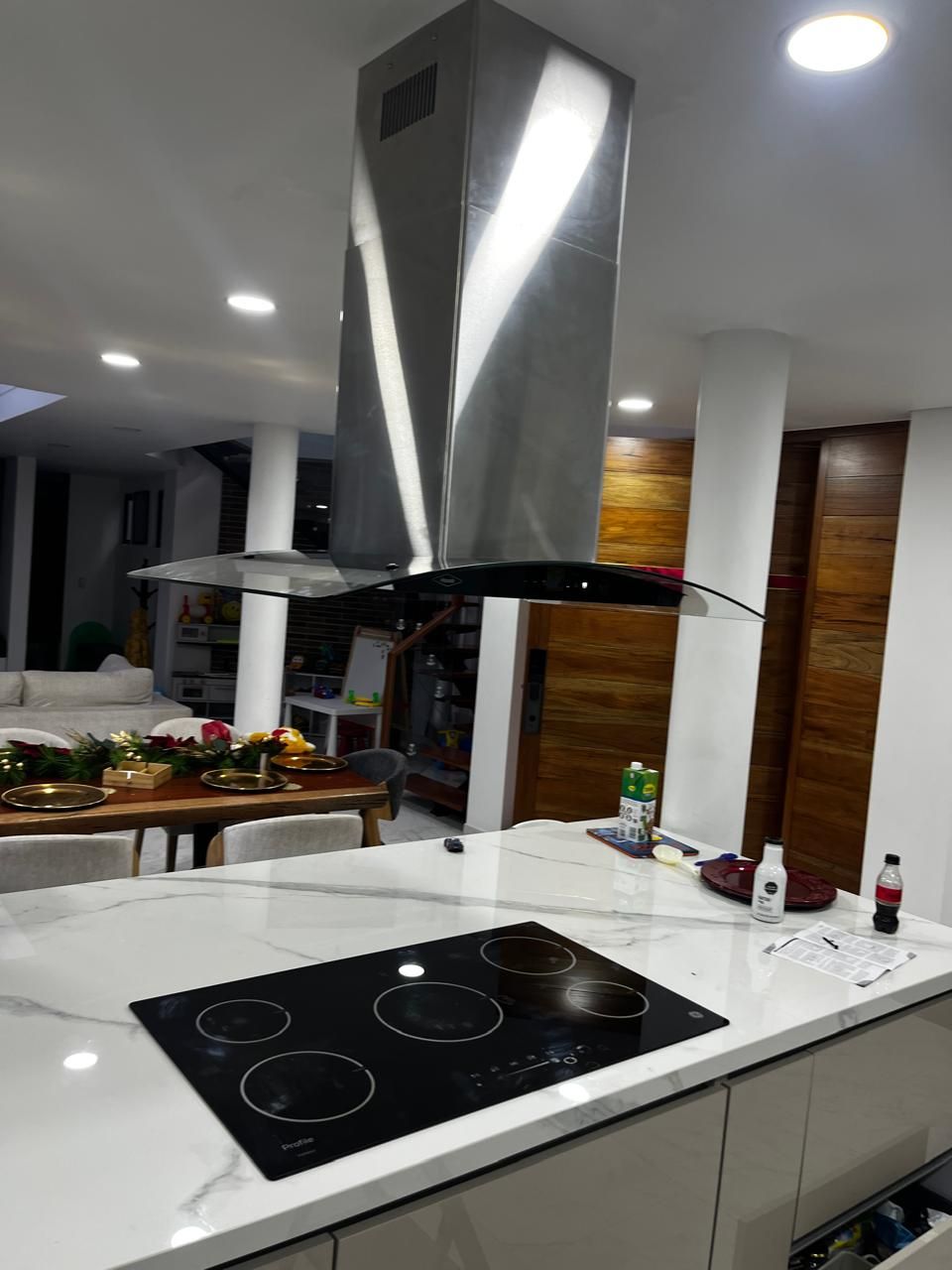 Una campana extractora de acero inoxidable cuelga sobre una placa de cocina de vidrio en una isla de cocina de mármol blanco.