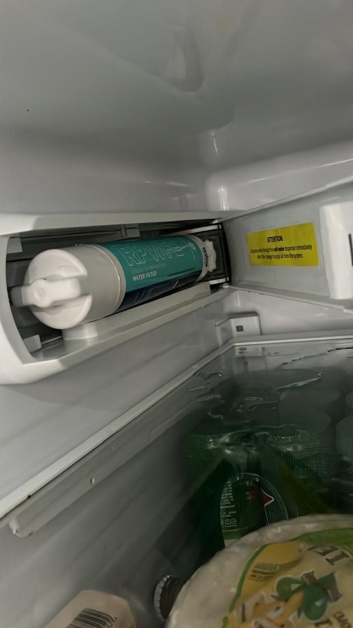 Un cartucho de filtro de agua cilíndrico azulado instalado dentro del compartimento superior de un refrigerador.