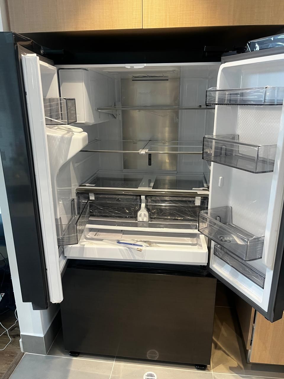Un refrigerador de puertas francesas, abierto, con estantes de vidrio ajustables y compartimentos de almacenamiento