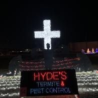 Illuminated white cross above a sign reading “HYDE’S TERMITES & PEST CONTROL” at night