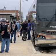 People standing beside a tour bus at a curb beside a sidewalk outside a building