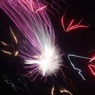 Abstract light streaks in pink, white, and red on a black background, like long-exposure fireworks.