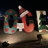Large festive letters spelling “OCA” with lights and decorations at night, plus a small sign in front.