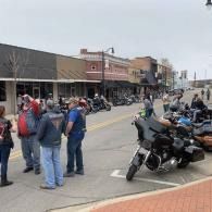 Street scene with parked motorcycles, several people, and storefronts under an overcast sky