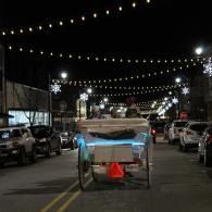 Horse-drawn cart with a glowing blue light on a decorated city street at night