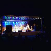 Outdoor stage performance at night with colorful lights and several performers on stage