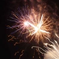 Bright fireworks exploding in the night sky with pink, white, and gold trails