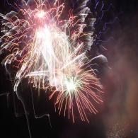 Colorful fireworks burst against a dark night sky, with white and pink sparks radiating outward.