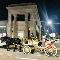 Horse-drawn carriage with passengers at night beside a lit stone building