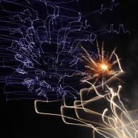 Abstract firework light trails and a bright orange spark on a dark background