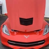 Red sports car front view with hood open, showing a Corvette emblem and black grille accents.