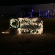 Illuminated Girl Scouts sign with holiday wreath at night, with arched purple-lit lights in the background