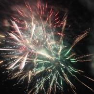 Colorful fireworks bursting in the night sky with green, white, and red trails
