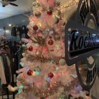 Pink Christmas tree with ornaments beside a “Rockin” sign in a dimly lit interior