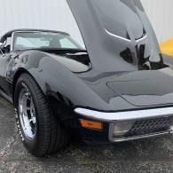Black classic sports car with raised hood, parked outdoors on wet pavement.
