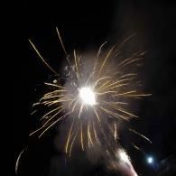 Bright white fireworks burst against a dark night sky, with sparks radiating outward.