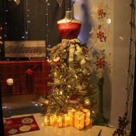 Decorated Christmas mannequin display with red dress, white skirt, and glowing lanterns in a window
