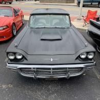 Black classic car with hood scoop parked at a car show, front view