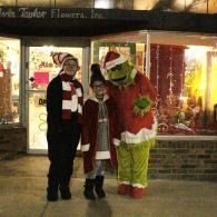 Three costumed people in winter outfits standing outside a flower shop, including a Grinch costume.