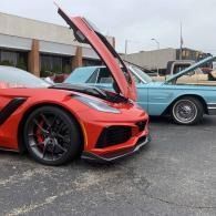 Red sports car with hood open parked beside a light blue classic convertible in a lot.