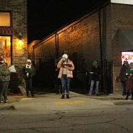 People standing outside a brick building at night, with one person centered under warm lights.