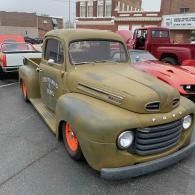 Olive-green vintage pickup truck with orange wheels parked at a car show