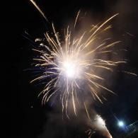 Bright fireworks burst in the night sky over a dark outdoor scene