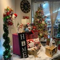 Christmas-themed living room with decorated tree, gifts, wreaths, and a vertical “HOME” sign
