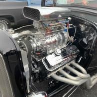 Polished chrome supercharged engine in a black classic car with exposed exhaust headers