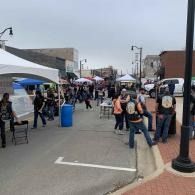 Outdoor street fair with tents, people walking, and a blue trash can along a closed-off street.