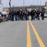 Group of people standing across a road between yellow centerlines, with motorcycles parked along the left side.