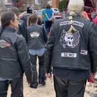Motorcycle club members in black leather jackets walking outdoors, one jacket reading “Ridge Runners” and “SE.MO MC”