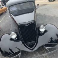 Front view of a glossy black vintage car with rounded fenders and chrome headlights.