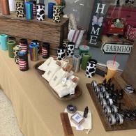 Table display of colorful cups, mugs, and jars with farmhouse decor in a home shop.