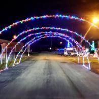 A road at night under colorful illuminated arch lights, with streetlights and a vehicle on the right.