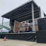 Outdoor stage with a roof, black skirting, and two people standing on it during setup