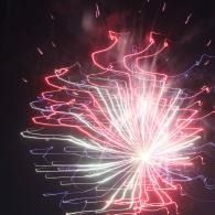 Pink and white fireworks burst against a dark night sky, with streaks radiating outward.