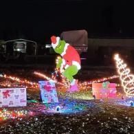 Christmas yard display with a Grinch figure, glowing lights, and wrapped gift decorations at night