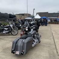 Black touring motorcycle parked on concrete at an outdoor motorcycle event, with tents and other bikes in the background