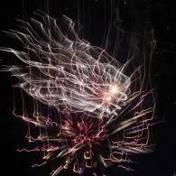 Abstract firework light trails on a black background, white and red streaks radiating in a burst.