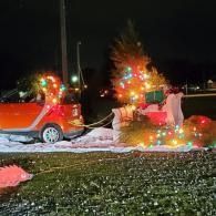 Two small red holiday-decorated cars glowing with colorful lights on a grassy lawn at night