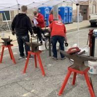 People working at an outdoor setup with red sawhorses and blue portable toilets in the background
