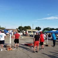 People in red and white shirts gathered outdoors near tables and tents on a sunny day.