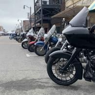 Row of parked motorcycles outside a building, with a large black bike in the foreground.