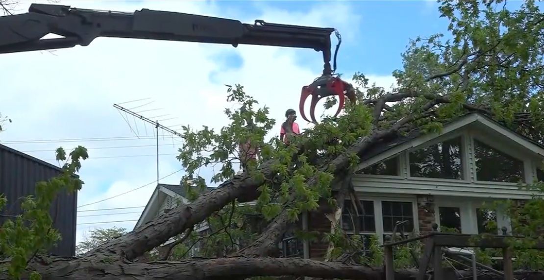 Crane lifting a fallen tree limb over a house amid storm damage