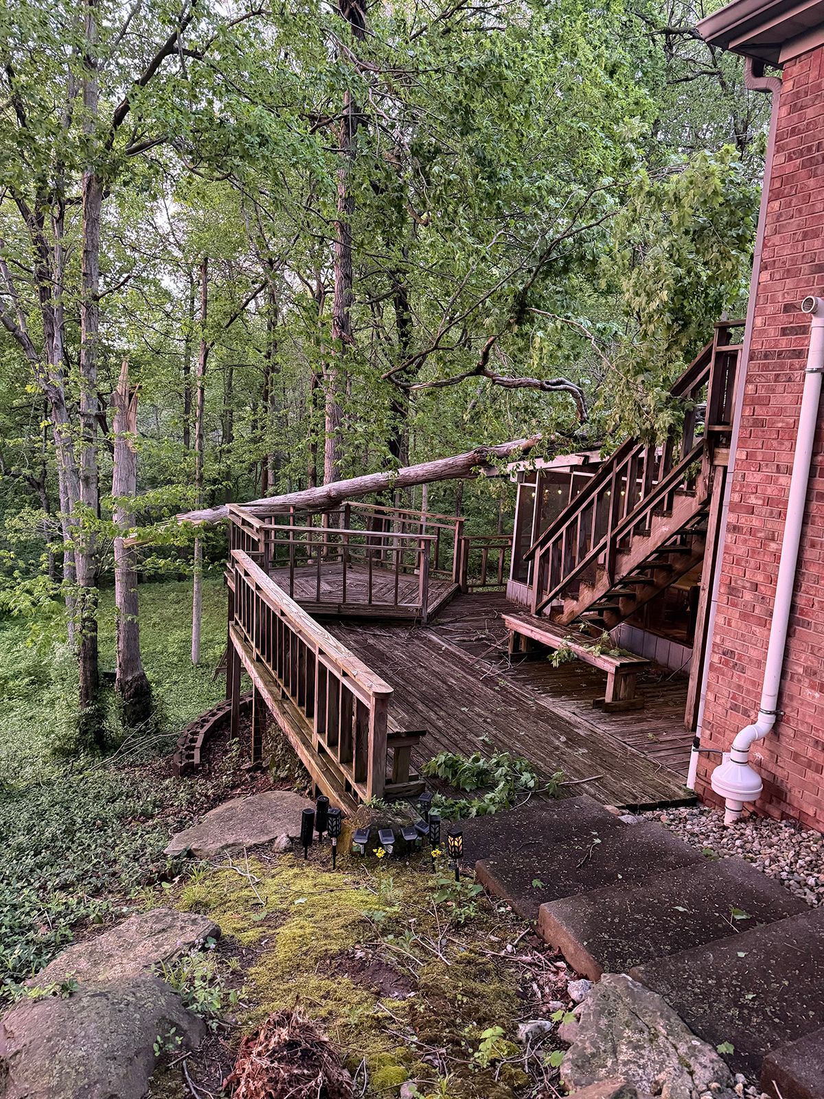 Wooden deck and stairs beside a red brick house, overlooking a leafy forest.