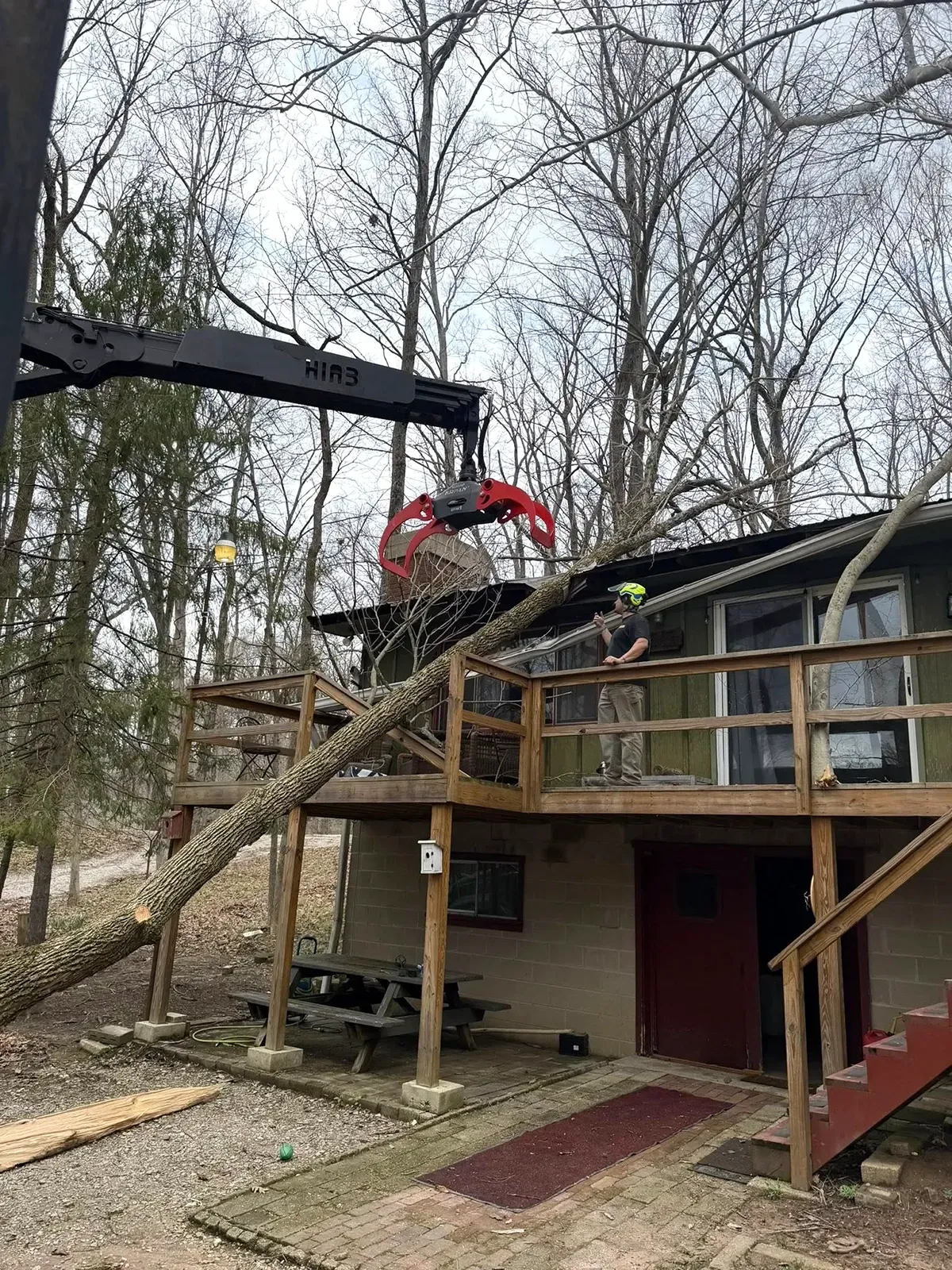 Outdoor structure with a red crane lifting debris above a deck and stairs in a wooded area